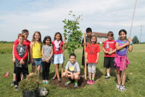 a picture of children posing next to a recently planted tree
