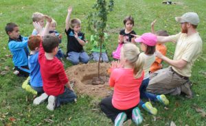picture of children and an educator sitting around a recently planted tree