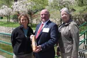 Award winner stands with Sally Claggett and Rebecca Hanmer in front of flowering trees